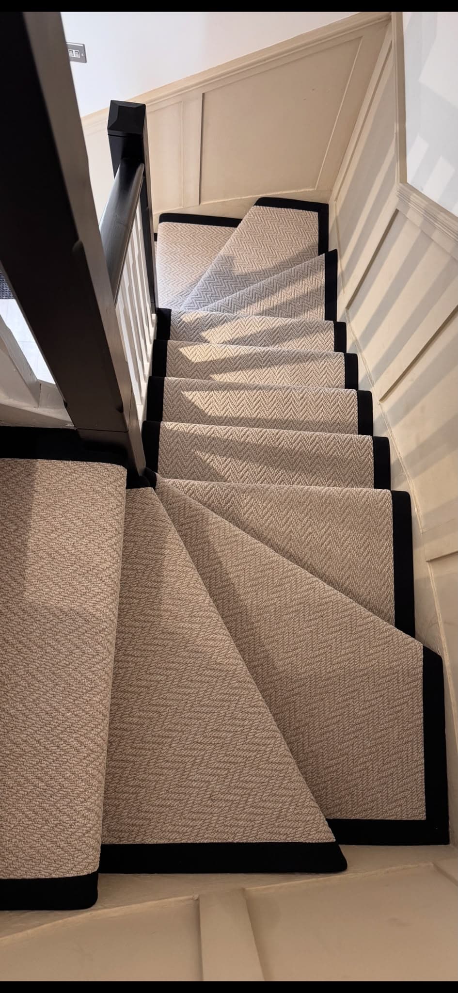 Herringbone-weave carpet with black border trim fitted on a curved staircase by Philip B Flooring