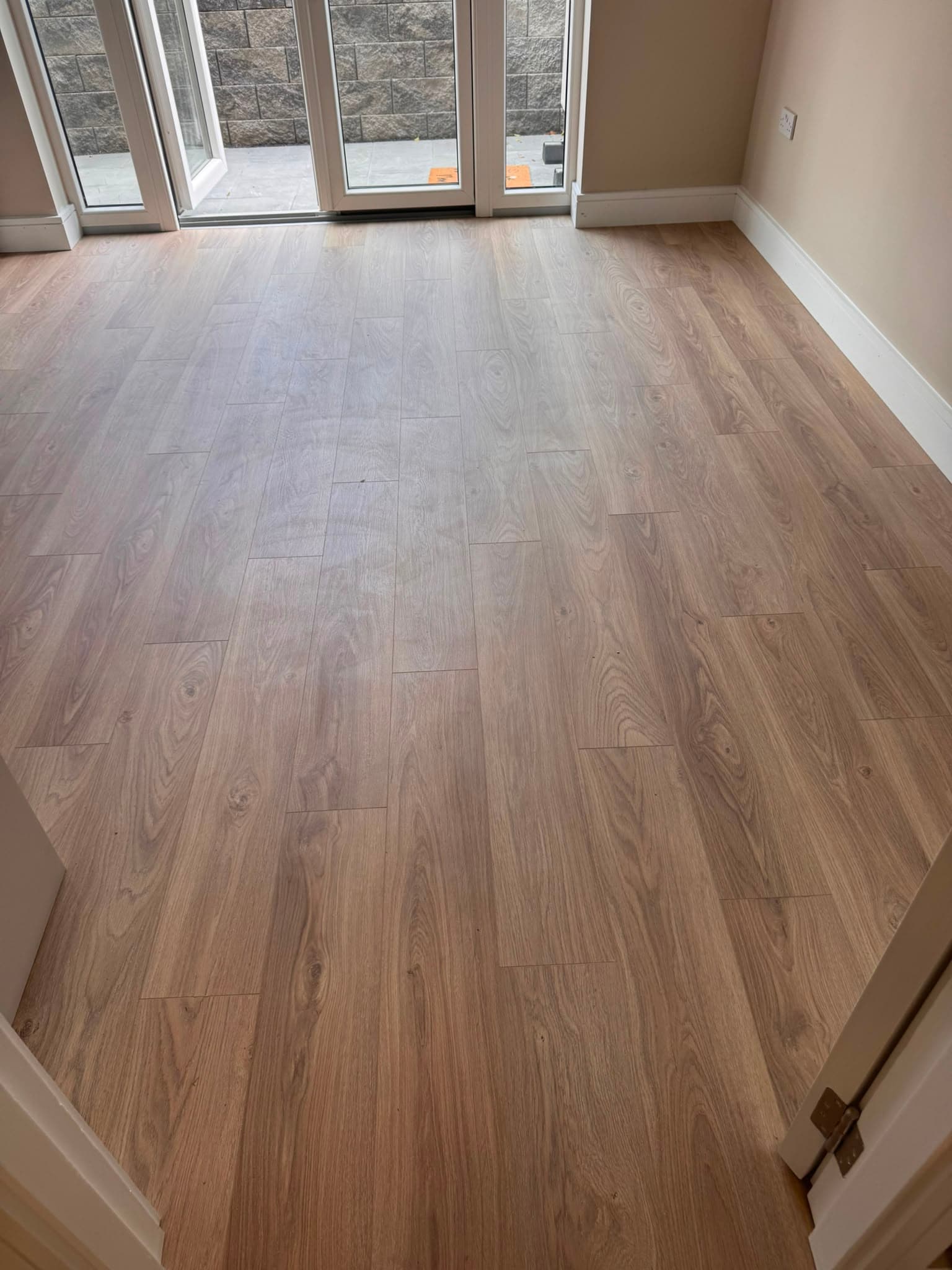 Pale oak-effect laminate flooring fitted in a bright room with patio doors